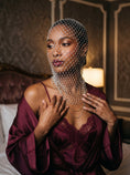 Cargar la imagen en la vista de la galería, Pearl net veil draping over the throat in low lamplight, worn over a burgundy satin slip