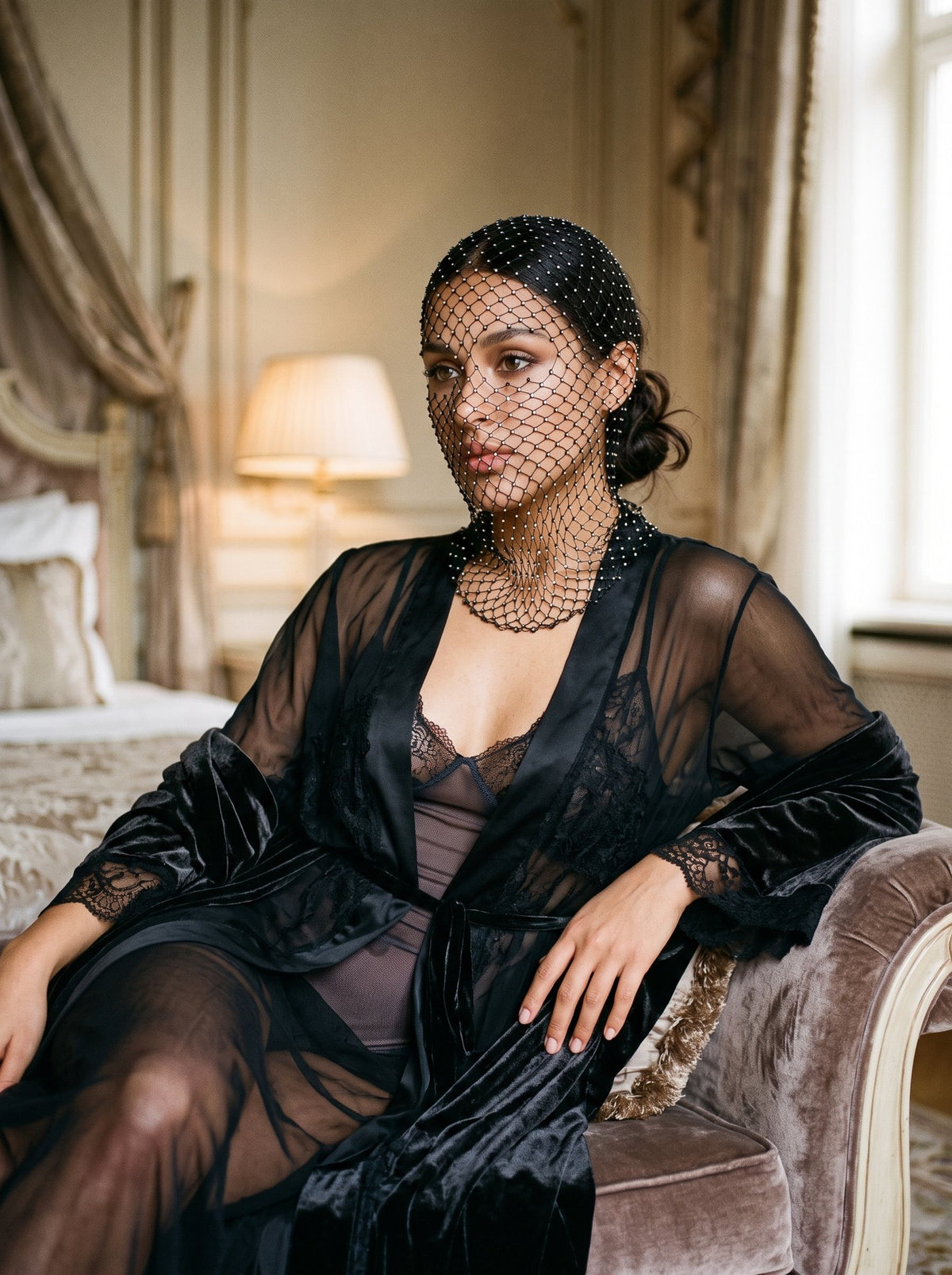 Black rhinestone net veil over face and throat, layered over a sheer robe and lace slip, seated indoors