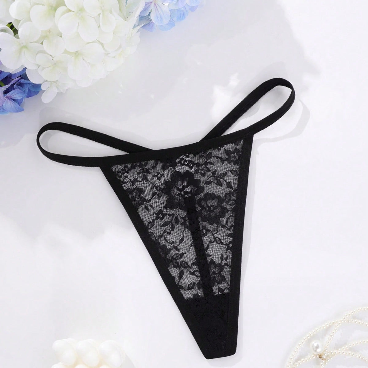 Black sheer floral lace G-string with metal heart ring, flat lay