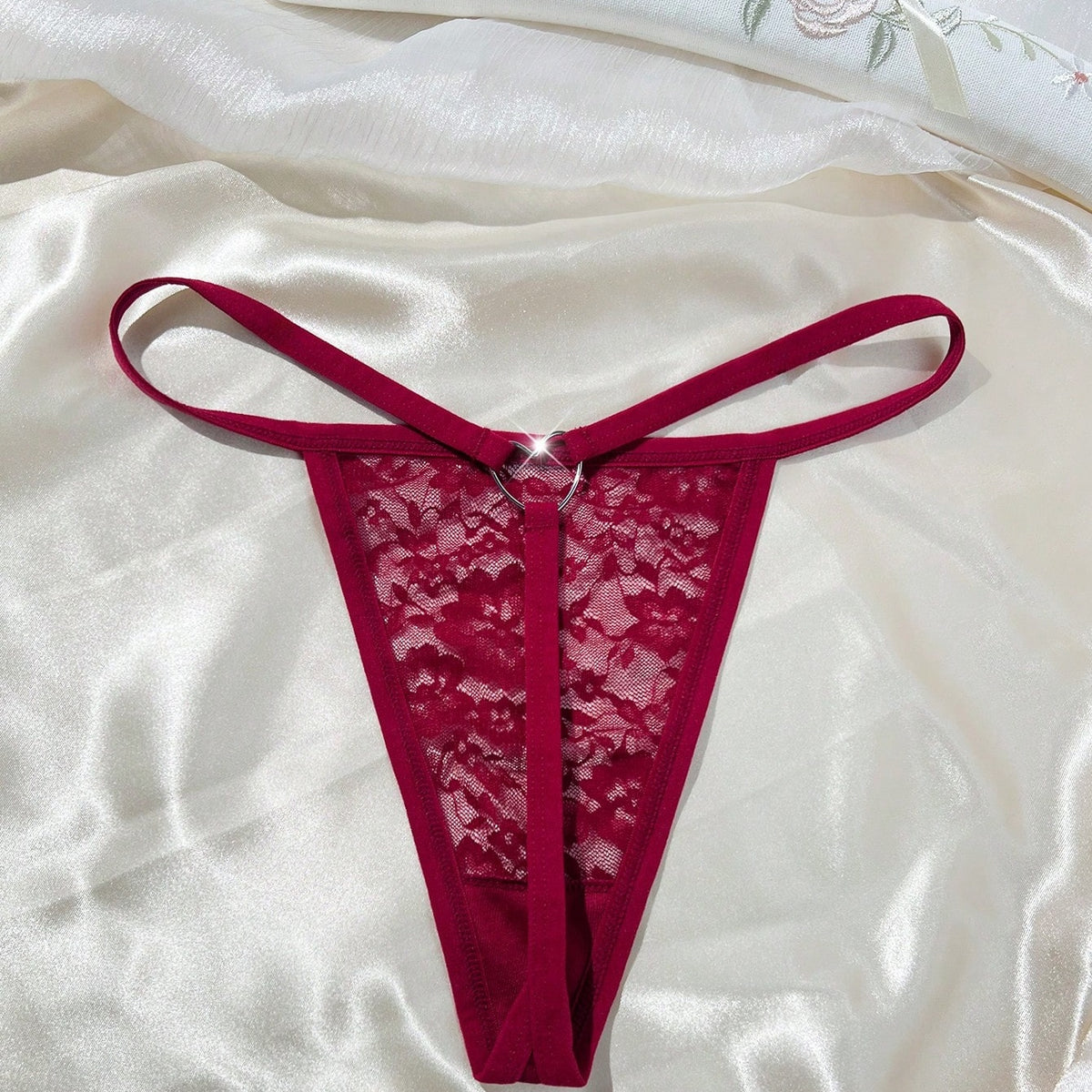Deep red sheer floral lace G-string with metal heart ring, flat lay