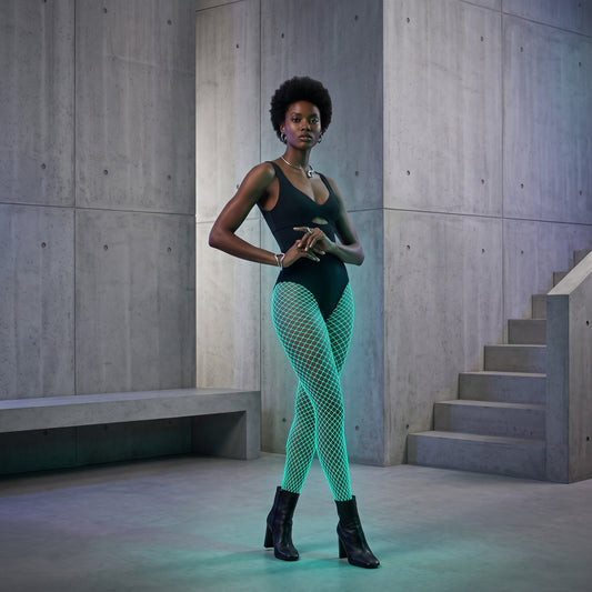Model in white fishnet tights glowing green, standing in a dark modern building at night