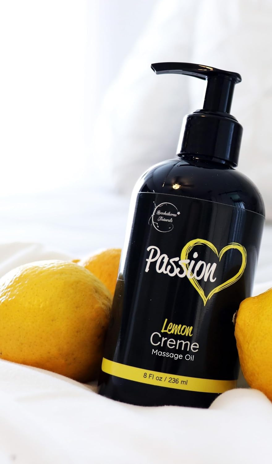 Massage oil bottle resting on white bedding between two lemons