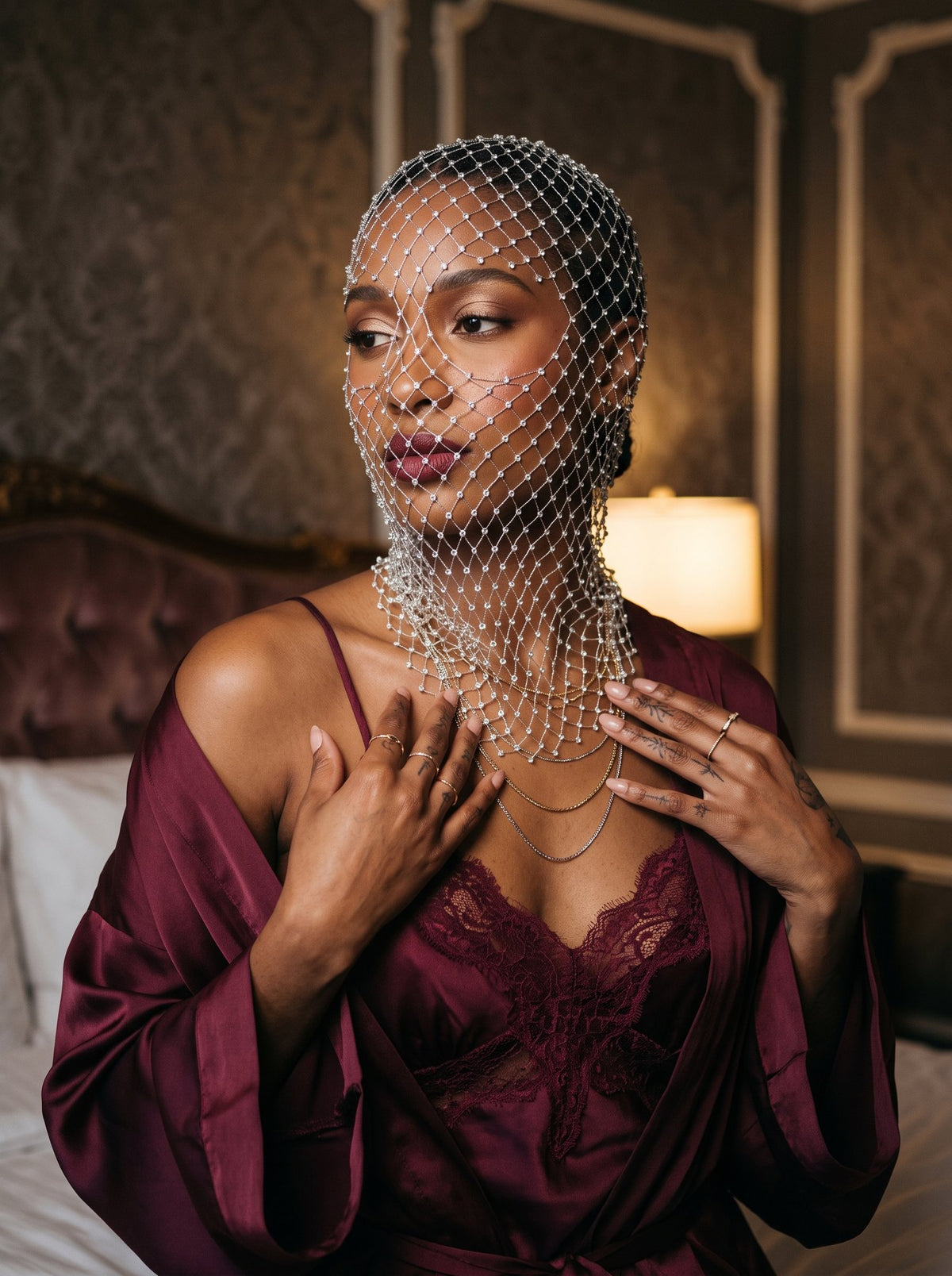 Pearl net veil draping over the throat in low lamplight, worn over a burgundy satin slip